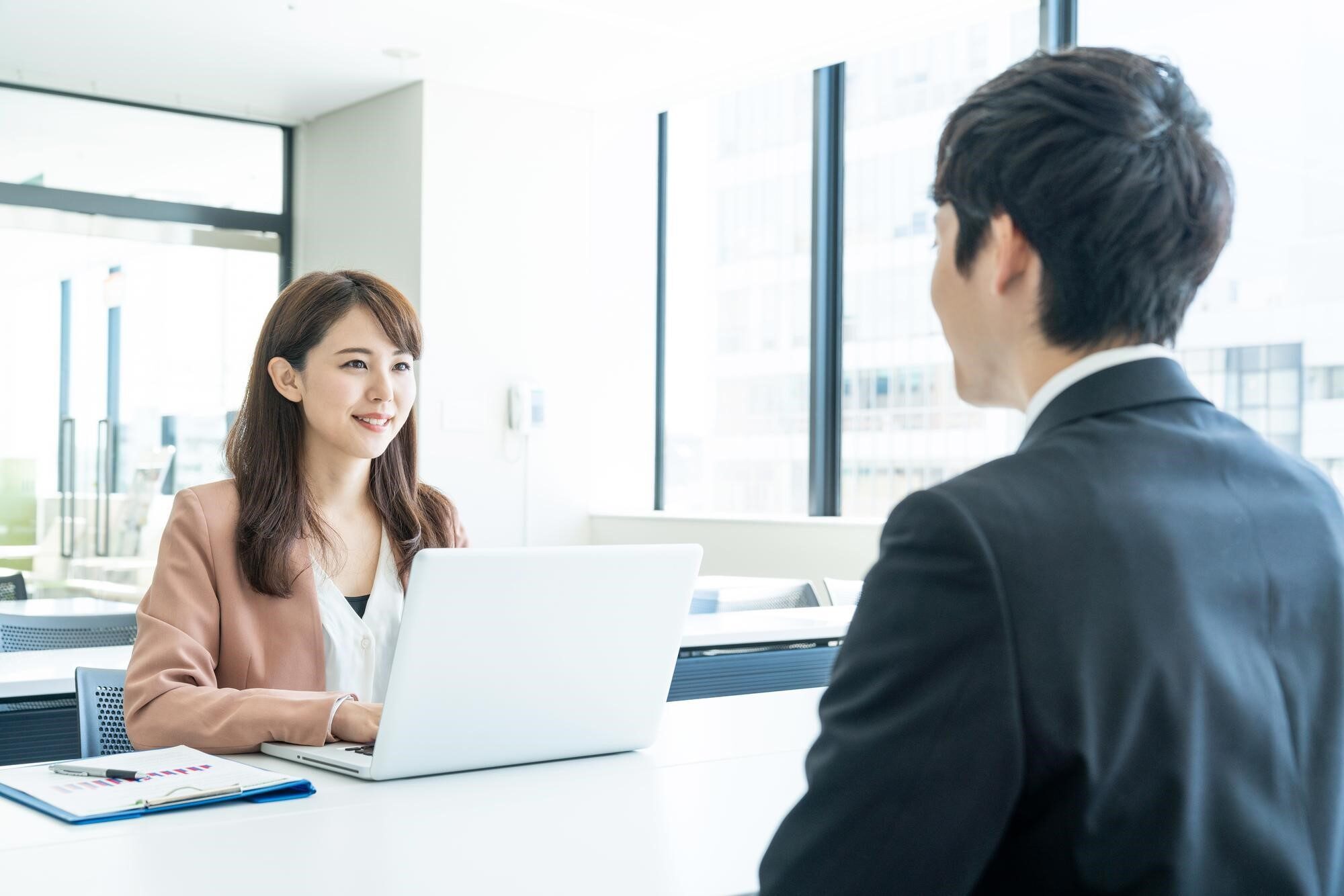 明るいオフィスでPCの前に座る女性と向かいに座るスーツ姿の男性