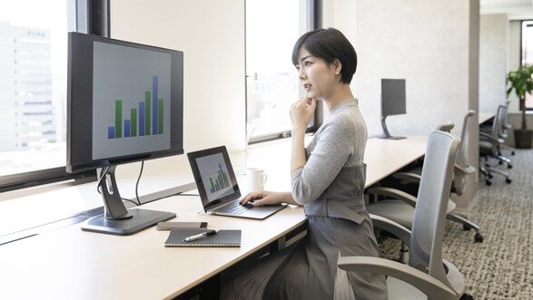 PCに表示されたデータを確認しながらデスクで何か考え事をしている女性