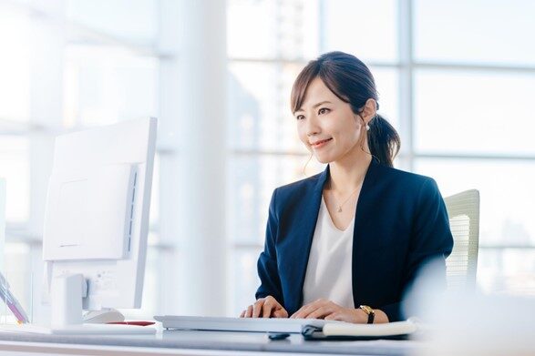 パソコンの前で笑顔で仕事をするスーツ姿の女性