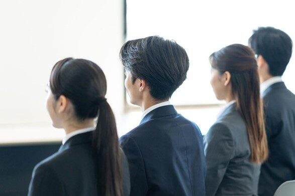 前を向き横並びで座っている男女4人のビジネスパーソンの後ろ姿
